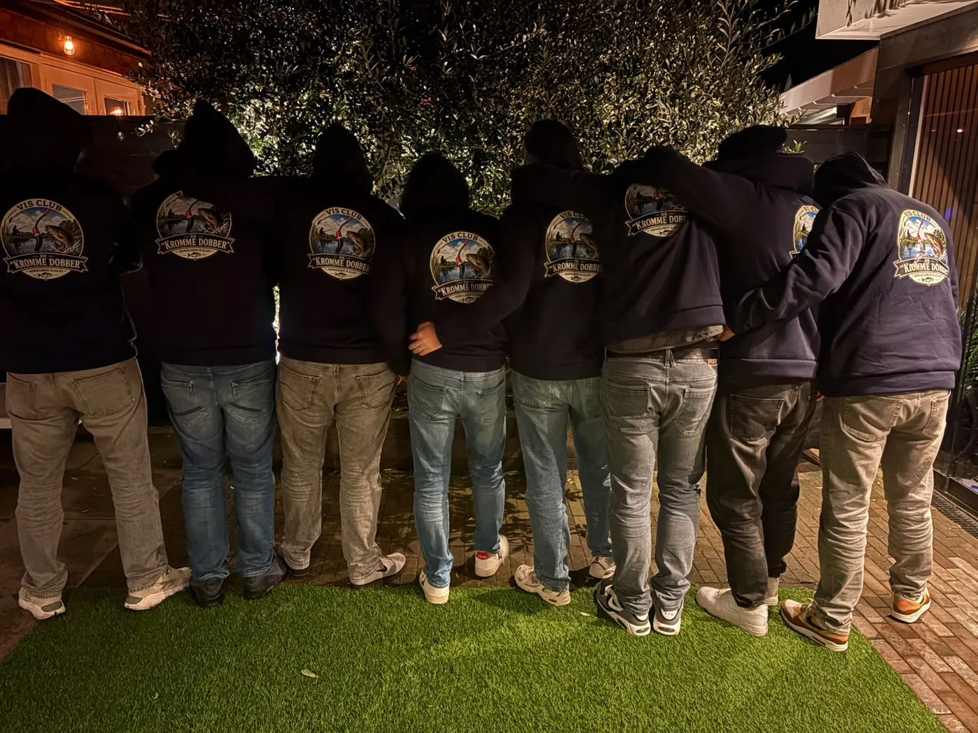 De leden van De Kromme Dobber op een rij, met de rug naar de camera in de clubhoodies